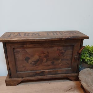 May include: A rectangular wooden bread bin with a dark brown finish. The top surface features the text FARM FRESH in dark lettering. The front door panel displays a printed illustration of several chickens and a rooster in a farmyard setting.