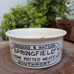 May include: A white ceramic pot with a black printed label that reads HORROCKS & WATSON SPRINGFIELD HOME POTTED MEATS SOUTHPORT inside an oval border. The container has a smooth finish and a small chip on the upper rim edge of the circular opening.