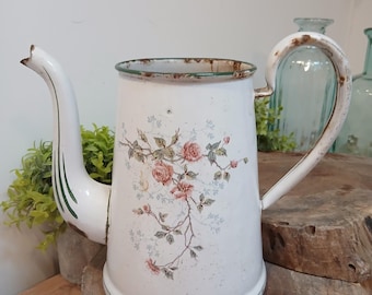 May include: A white enamel coffee pot featuring a floral pattern of pink roses and green leaves. The pot has a curved handle, a long spout, and visible signs of wear with rust along the rim, base, and handle, showing a distressed finish.