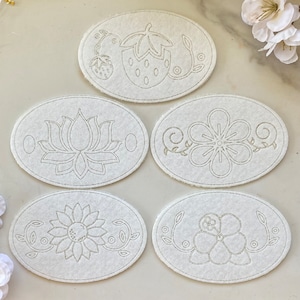 May include: Five white felt oval-shaped patches with different embroidered floral designs. The designs include a strawberry, a lotus flower, a simple flower with vines, a sunflower with vines, and a small flower with vines.