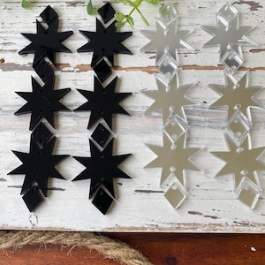 May include: Four sets of star-shaped acrylic components arranged in two columns. The left column features two pairs of solid black star and diamond shapes, while the right column displays two pairs of reflective silver mirror star and diamond shapes.