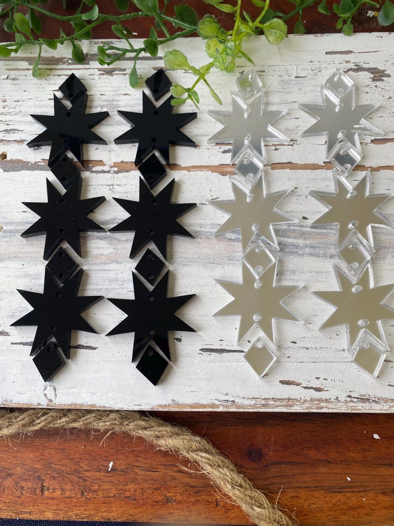 May include: Four sets of star-shaped acrylic components arranged in two columns. The left column features two pairs of solid black star and diamond shapes, while the right column displays two pairs of reflective silver mirror star and diamond shapes.