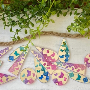 May include: A collection of assorted acrylic shapes including teardrops, circles, and elongated triangles featuring a reflective mirror finish. Each piece is decorated with a repeating pattern of small butterflies and geometric diamond motifs in gradients of pink, purple, and blue.