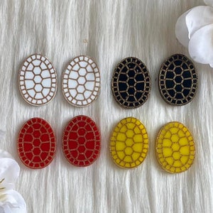 May include: Six pairs of oval-shaped earrings with a turtle shell design. The earrings are in white, black, red, and yellow.
