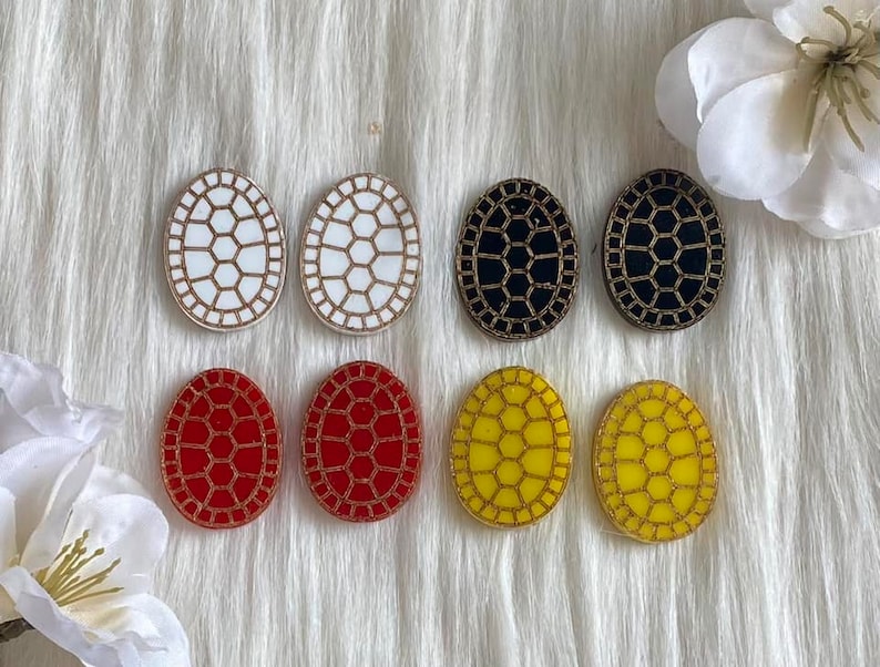 May include: Six pairs of oval-shaped earrings with a turtle shell design. The earrings are in white, black, red, and yellow.