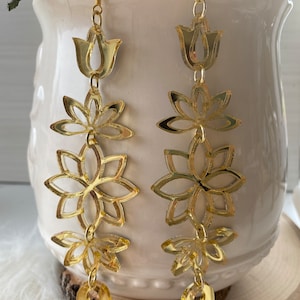 May include: Gold tone earrings with a floral design. The earrings feature a series of cascading flowers, each with a delicate, intricate pattern. The flowers are connected by small chains, creating a flowing, elegant look.