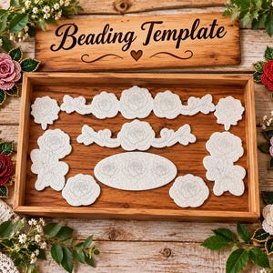 Könnte beinhalten: Ein Holztablett mit weißen Filz-Perlstickvorlagen mit Rosenmotiven, darunter florale Streifen, einzelne Blüten und ein ovales Stück. Ein Holzschild darüber trägt die Aufschrift Beading Template mit einem Herzsymbol.