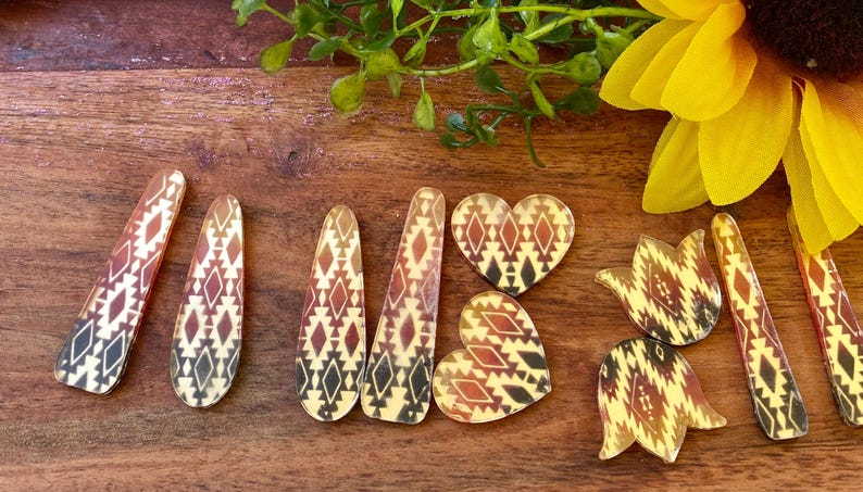 May include: A collection of flat, decorative acrylic shapes featuring a repeating geometric pattern in shades of cream, brown, and black. The set includes elongated teardrop pieces, two heart-shaped pieces, and two tulip-shaped pieces with smooth edges.