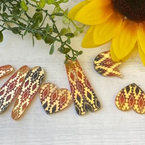 May include: A collection of hair clips and earrings featuring a repeating geometric pattern in shades of red, black, and cream. The set includes various shapes such as elongated rectangles, hearts, and tulip-like forms with a glossy finish.