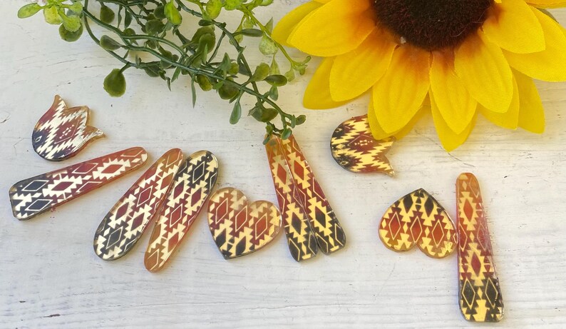 May include: A collection of hair clips and earrings featuring a repeating geometric pattern in shades of red, black, and cream. The set includes various shapes such as elongated rectangles, hearts, and tulip-like forms with a glossy finish.