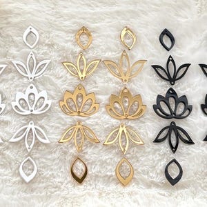 May include: A collection of laser-cut acrylic components in white, gold, and black. The set includes various lotus flower shapes, petal motifs, and teardrop-shaped connectors, each featuring small pre-drilled holes for assembly into jewelry pieces.