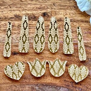May include: A collection of ten flat, gold-toned decorative shapes featuring a repeating geometric diamond pattern. The set includes six elongated, tapered strips, two heart-shaped pieces, and two tulip-shaped pieces, all with a consistent metallic finish.