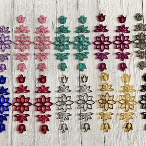 May include: Assortment of 10 pairs of earrings featuring a variety of colors and designs. Each pair includes a small flower-shaped earring and a larger flower-shaped earring. The colors include purple, pink, teal, red, silver, gold, and black.