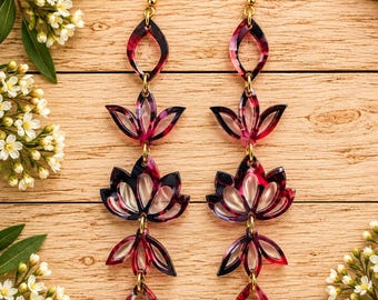 May include: A pair of long dangle earrings featuring a multi-layered design with a dark pink and black tortoiseshell pattern. Each earring consists of five connected acrylic segments in geometric and floral shapes, suspended from gold-tone hooks.