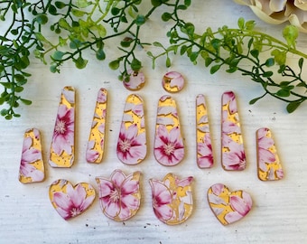 May include: A collection of various flat, decorative shapes featuring a pink and white floral pattern on a gold background. The set includes rectangular, heart-shaped, tulip-shaped, and circular pieces with smooth, glossy surfaces and rounded edges.