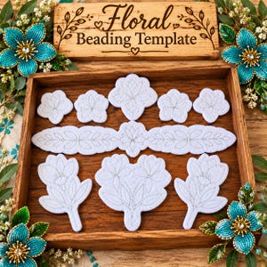 May include: A wooden tray containing white felt shapes with silver stitched floral outlines. A wooden sign above reads Floral Beading Template. Two turquoise beaded flowers with gold centers are placed at the top and bottom corners of the tray.