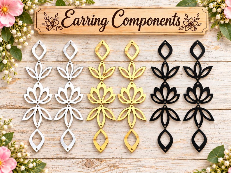 May include: Six vertical earring components arranged in pairs of silver, gold, and black. Each piece features a repeating geometric floral pattern with small circular holes for assembly. A wooden sign at the top reads Earring Components.