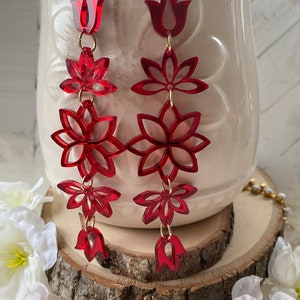 May include: A pair of long red dangle earrings with a floral design. Each earring features a series of red flowers and a red tulip at the bottom.