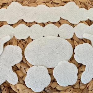 May include: A set of white felt appliques featuring floral and hummingbird designs. The appliques are ideal for crafting projects, such as decorating clothing, bags, or home decor.