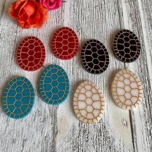 May include: Seven oval-shaped resin earrings with a geometric pattern. The earrings are in various colors, including red, black, white, blue, and turquoise.