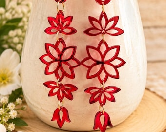 May include: A pair of long dangle earrings featuring a vertical arrangement of four red, translucent, laser-cut floral shapes connected by small gold-toned metal jump rings, suspended from gold-toned metal earring hooks.