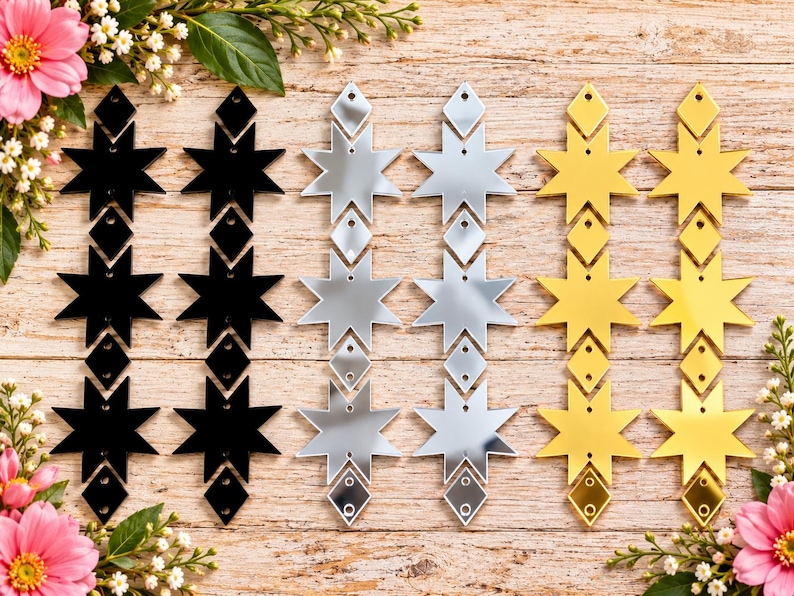 May include: Six vertical earring components arranged in three pairs of black, silver, and gold mirrored acrylic. Each piece features a repeating geometric design of three eight-pointed stars interspersed with small diamond-shaped connectors.