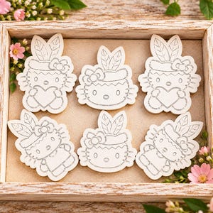 May include: Six white wooden cutouts featuring the character Hello Kitty. Four cutouts depict the character holding a heart, while two cutouts show only the head of the character. Each figure includes a bow and two leaf-shaped ears on top.