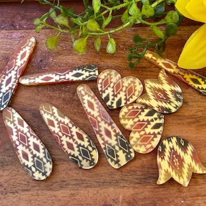 May include: A collection of hair clips featuring a repeating geometric pattern in shades of brown, black, and cream. The set includes various shapes such as elongated rectangles, hearts, and tulip-like forms, all displaying a consistent southwestern-inspired motif.