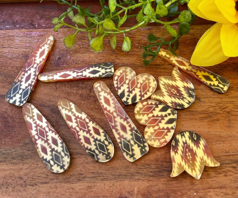 May include: A collection of hair clips featuring a repeating geometric pattern in shades of brown, black, and cream. The set includes various shapes such as elongated rectangles, hearts, and tulip-like forms, all displaying a consistent southwestern-inspired motif.