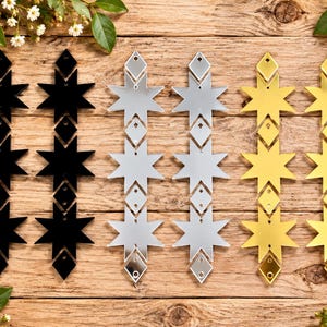 May include: Six vertical hanging ornaments arranged in three pairs of black, silver, and gold colors. Each ornament features a repeating pattern of three eight-pointed stars connected by small diamond-shaped spacers, each with a pre-drilled hole.