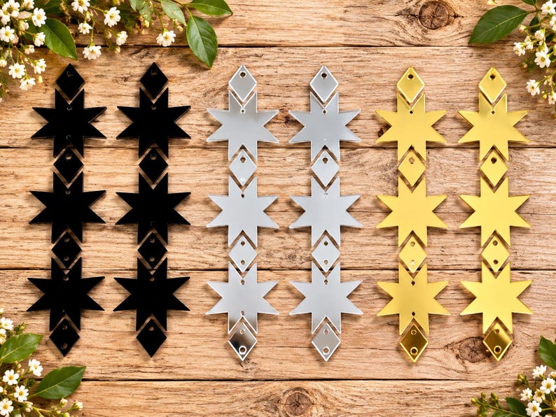 May include: Six vertical hanging ornaments arranged in three pairs of black, silver, and gold colors. Each ornament features a repeating pattern of three eight-pointed stars connected by small diamond-shaped spacers, each with a pre-drilled hole.