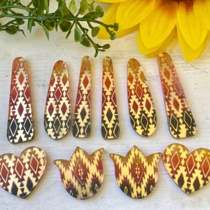 May include: A collection of ten acrylic craft pieces featuring a geometric pattern in shades of red, orange, and black. The set includes six elongated teardrop shapes and four pieces shaped like hearts and tulips, all with a smooth, glossy finish.