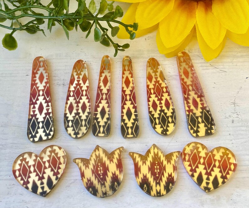 May include: A collection of ten acrylic craft pieces featuring a geometric pattern in shades of red, orange, and black. The set includes six elongated teardrop shapes and four pieces shaped like hearts and tulips, all with a smooth, glossy finish.