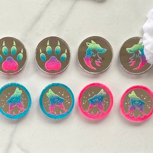May include: Eight iridescent holographic stickers with different designs. The stickers feature a paw print, a wolf howling at the moon, and a wolf head. The stickers are on a white background.