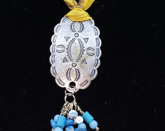 This pretty pewter pendent is hung from a orange and brown Silk ribbon.  Beautiful Turquoise beads hang from the pendent.