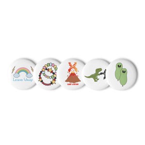 Puede incluir: Cinco chapas redondas con diseños distintos: un arcoíris con el texto Legend Valley, una pulsera de cuentas coloridas, un volcán con el texto Lost Lands, un dinosaurio verde y dos figuras alienígenas verdes sobre un fondo blanco.