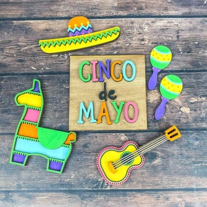 May include: A wooden sign with the text "CINCODEMAYO" in colorful letters, surrounded by wooden cutouts of a guitar, maracas, a sombrero, and a pinata.