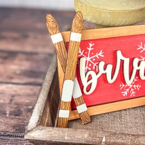 May include: Two wooden skis with white accents, resting on a wooden tray with a red sign that says "burr".