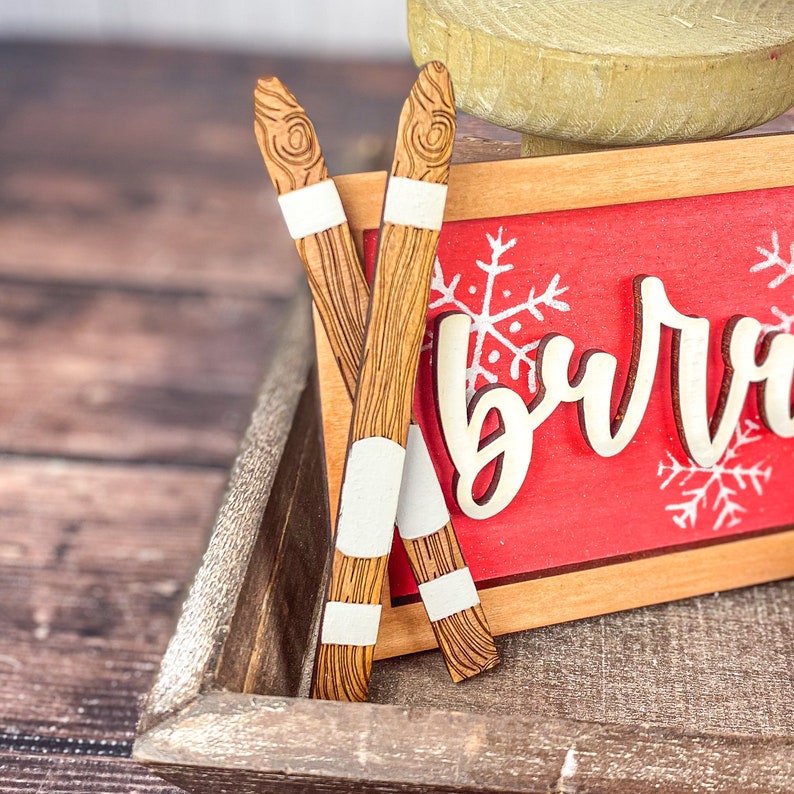 May include: Two wooden skis with white accents, resting on a wooden tray with a red sign that says "burr".