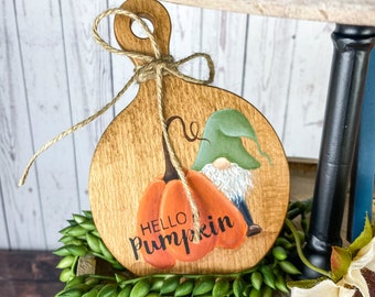 Może przedstawiać: Drewniana deska do krojenia z namalowanym gnomem i dynią. Dynia jest pomarańczowa i ma namalowane słowa "Hello Pumpkin". Gnom nosi zielony kapelusz i ma białą brodę.