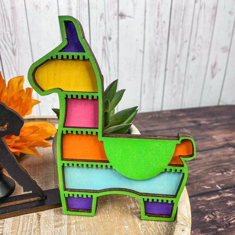 May include: A colorful wooden llama pinata with a green, blue, orange, pink, and yellow design. The pinata is shaped like a llama with a long neck and a small head.