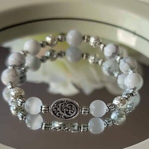 May include: A white and silver beaded bracelet with a silver charm featuring a tree design.