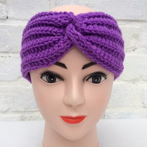 May include: Purple crocheted headband with a knotted design. The headband is worn on a mannequin head.