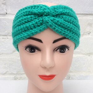 May include: A teal blue crocheted headband with a twist design. The headband is on a mannequin head.