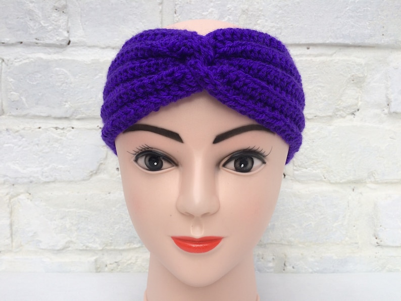 May include: Purple crocheted headband with a twisted knot design. The headband is worn on a mannequin head.