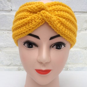 May include: A yellow crocheted headband with a twisted knot design. The headband is worn on a mannequin head.