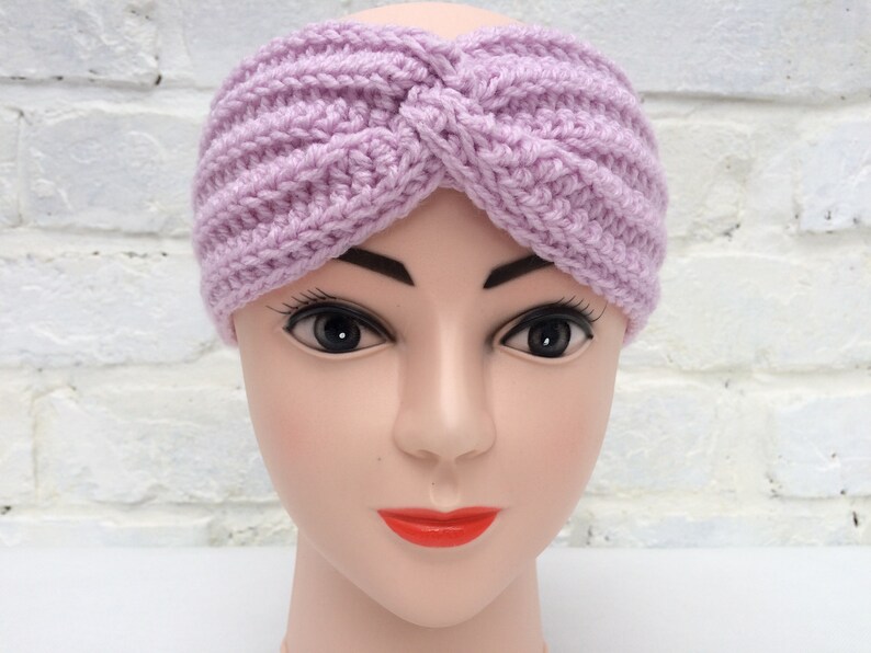 May include: A lavender crocheted headband with a twisted knot design. The headband is worn on a mannequin head.