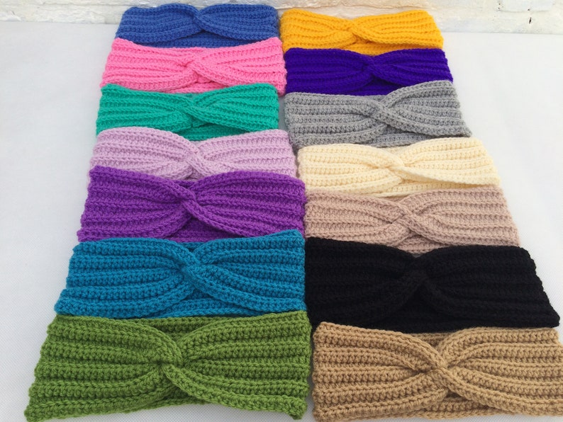 May include: A collection of 14 crocheted headbands in various colors, including pink, purple, teal, green, beige, and black. The headbands are all made with a twisted knot design.