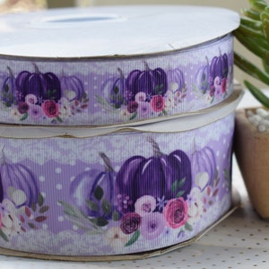 May include: Two spools of purple and white ribbon with a floral and pumpkin design. The ribbon has a white lace trim and white polka dots.