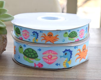 May include: Two spools of blue ribbon with a sea life pattern. The ribbon features seahorses, turtles, octopuses, and seashells.